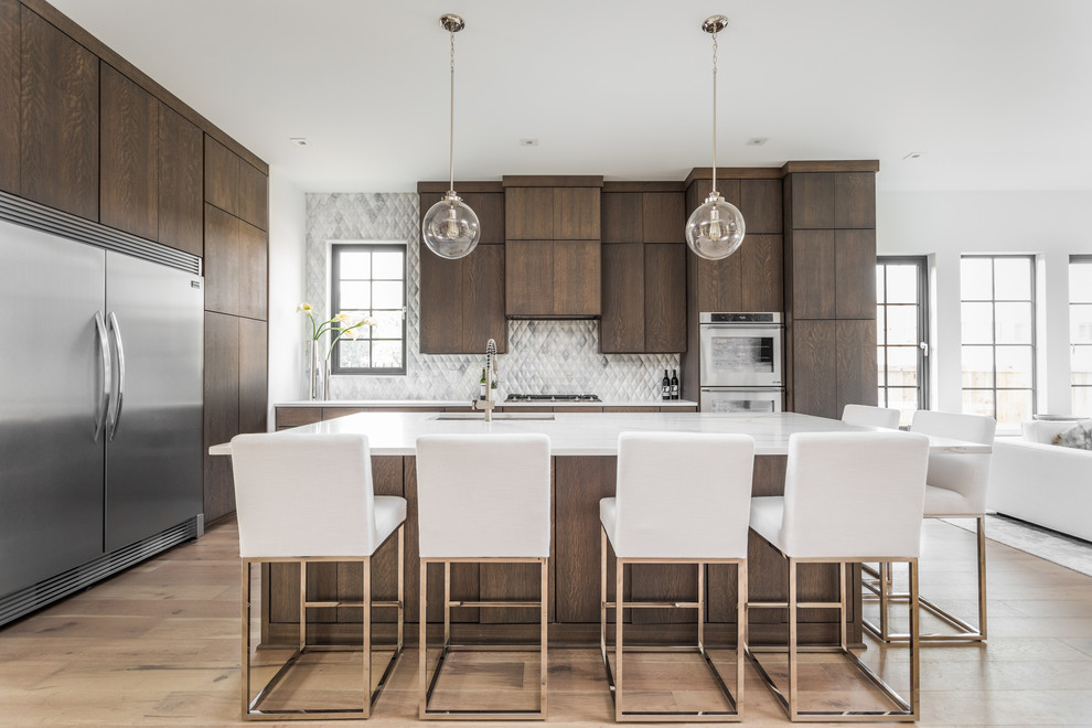 Photo of a contemporary open plan kitchen in Indianapolis with an undermount sink, flat-panel cabinets, dark wood cabinets, metallic splashback, stainless steel appliances, light hardwood floors, with island, beige floor and white benchtop.