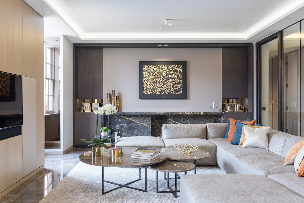 Expansive contemporary formal open concept living room in London with grey walls, marble floors, a stone fireplace surround and a wall-mounted tv.