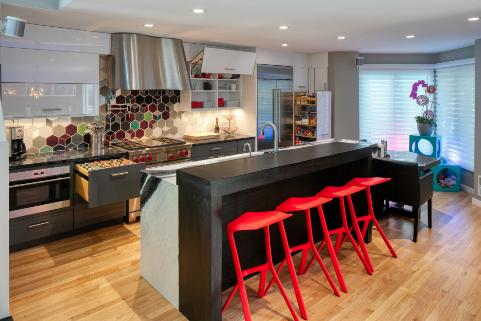 Example of a large trendy galley light wood floor eat-in kitchen design in Minneapolis with an undermount sink, flat-panel cabinets, gray cabinets, quartz countertops, mosaic tile backsplash, stainless steel appliances, an island and black countertops
