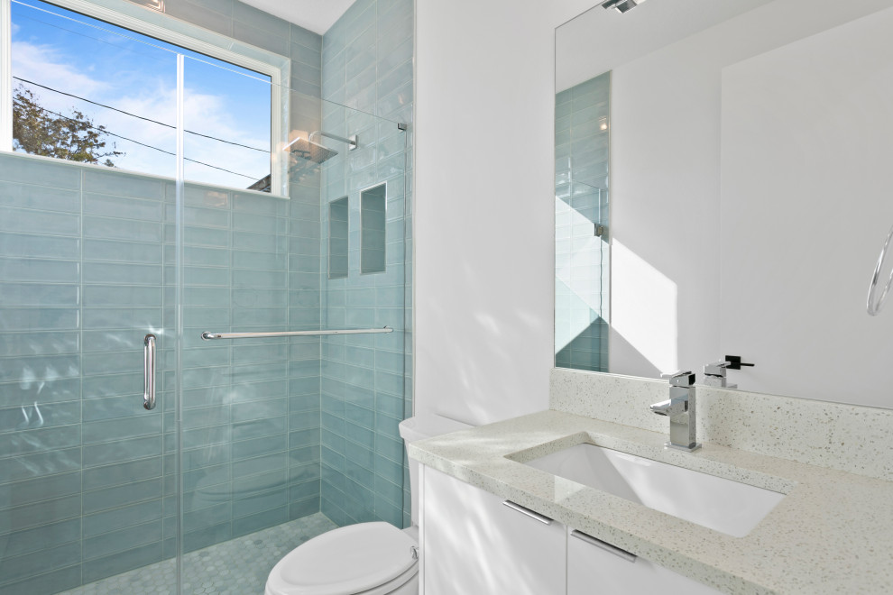 Exempel på ett litet modernt vit vitt badrum med dusch, med släta luckor, vita skåp, en kantlös dusch, en toalettstol med separat cisternkåpa, blå kakel, keramikplattor, vita väggar, klinkergolv i keramik, ett undermonterad handfat, bänkskiva i kvarts, blått golv och dusch med gångjärnsdörr