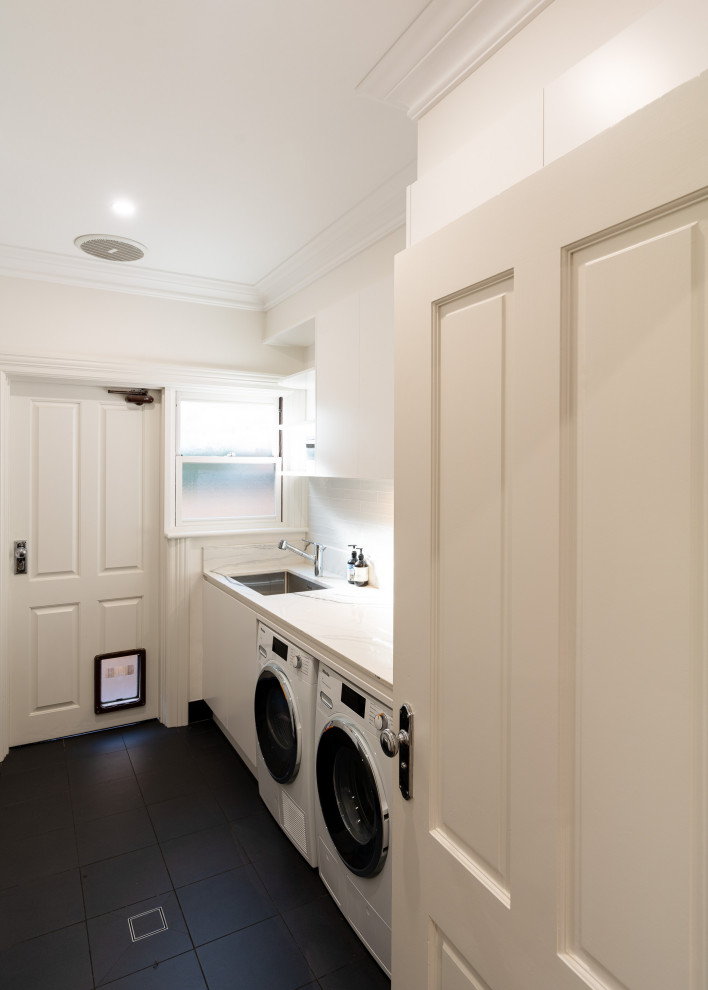 Inspiration for a modern single-wall separated utility room in Sydney with a submerged sink, flat-panel cabinets, white cabinets, engineered stone countertops, white splashback, white walls, ceramic flooring, a side by side washer and dryer, black floors and white worktops.