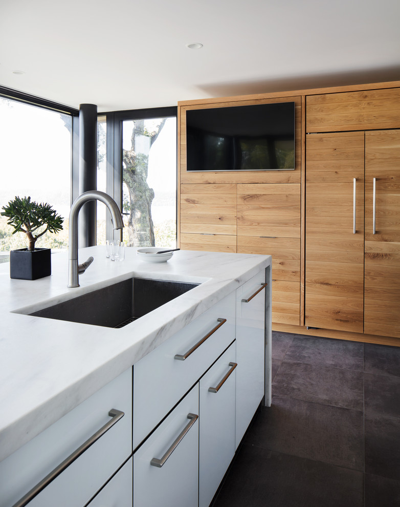 This is an example of a large contemporary l-shaped eat-in kitchen in New York with flat-panel cabinets, light wood cabinets, marble benchtops, white splashback, marble splashback, panelled appliances, porcelain floors, with island and white benchtop.