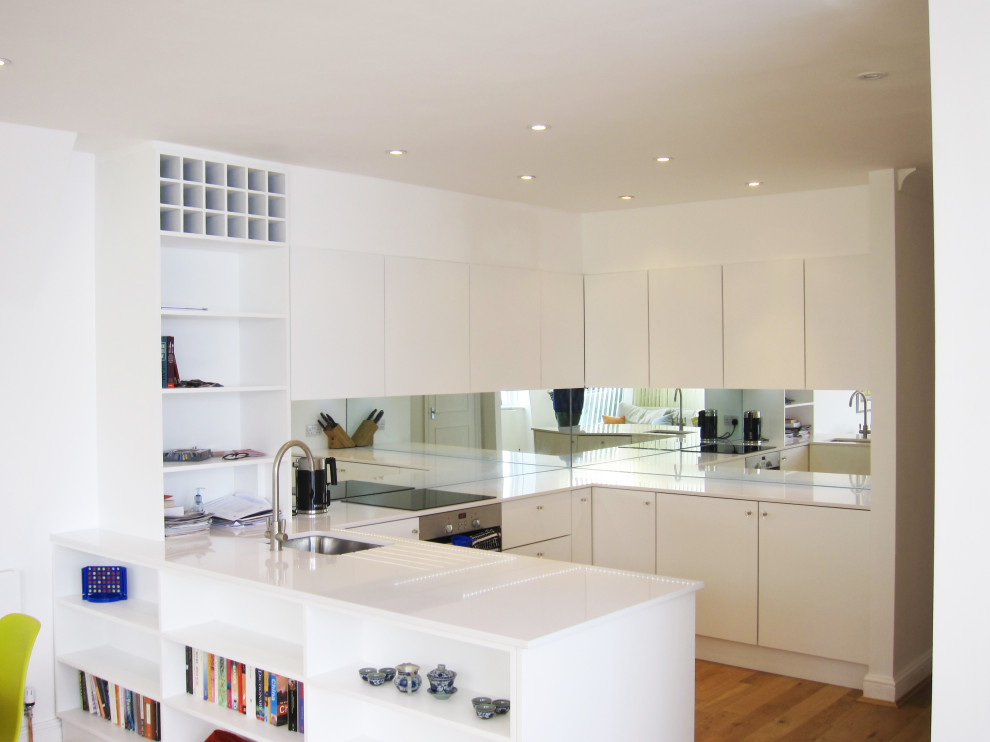 Inspiration for a mid-sized modern u-shaped eat-in kitchen in London with a single-bowl sink, quartzite benchtops, metallic splashback, mirror splashback, white appliances, light hardwood floors, with island and white benchtop.