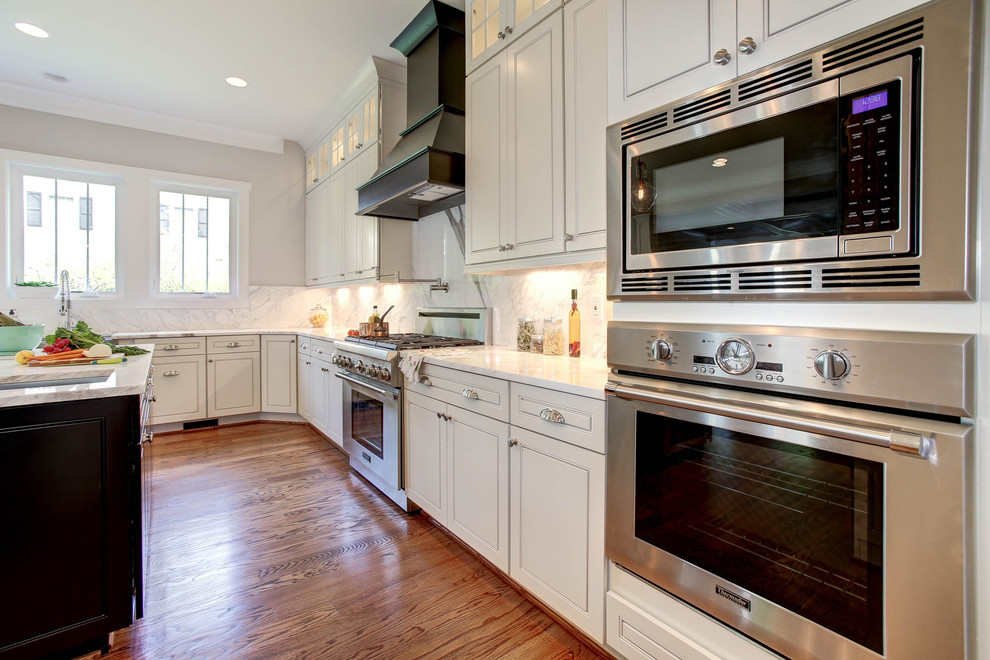 Example of a large transitional u-shaped medium tone wood floor eat-in kitchen design in DC Metro with a farmhouse sink, raised-panel cabinets, white cabinets, marble countertops, white backsplash, stone slab backsplash, stainless steel appliances and an island