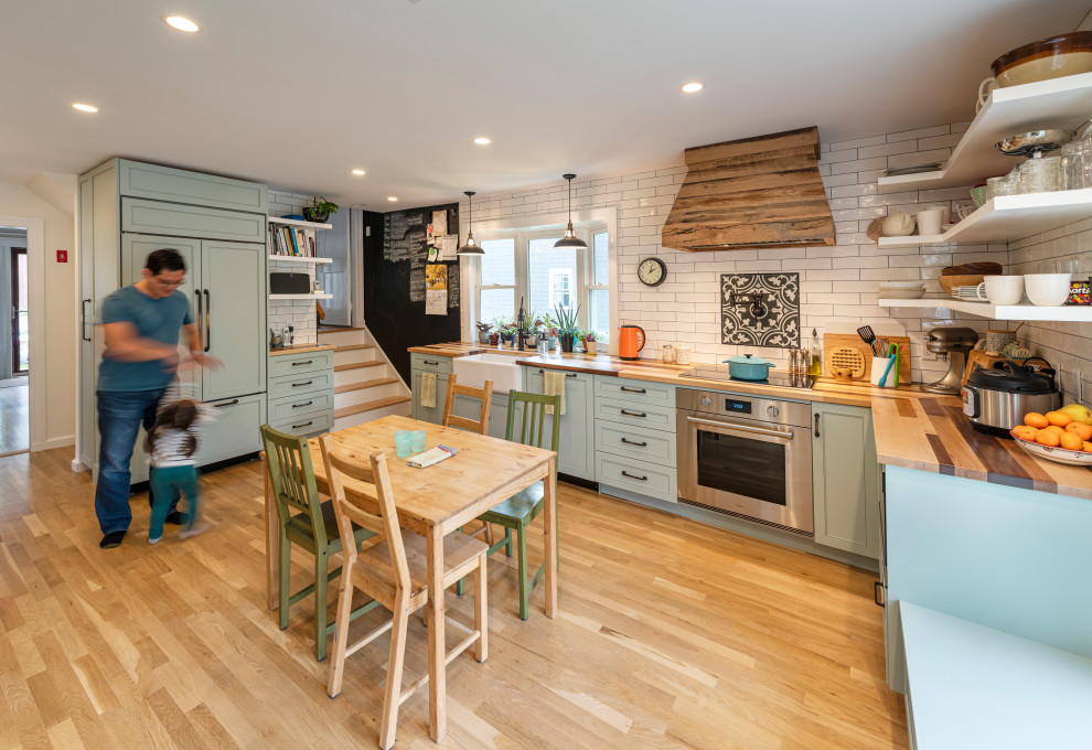 Photo of a mid-sized transitional l-shaped eat-in kitchen in Boston with a farmhouse sink, shaker cabinets, wood benchtops, white splashback, subway tile splashback, panelled appliances, light hardwood floors, no island, beige floor, beige benchtop and grey cabinets.