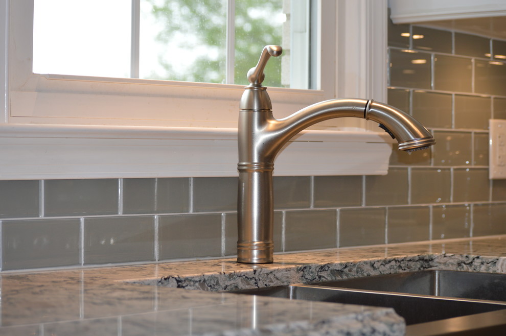 Example of a large transitional u-shaped ceramic tile and gray floor home design design with a farmhouse sink, raised-panel cabinets, white cabinets, quartz countertops, gray backsplash, glass tile backsplash, stainless steel appliances and an island