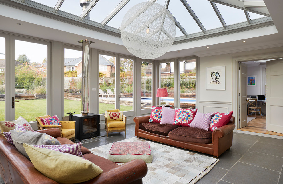 This is an example of a mid-sized eclectic sunroom in Essex with a wood stove, a glass ceiling, grey floor and a metal fireplace surround.
