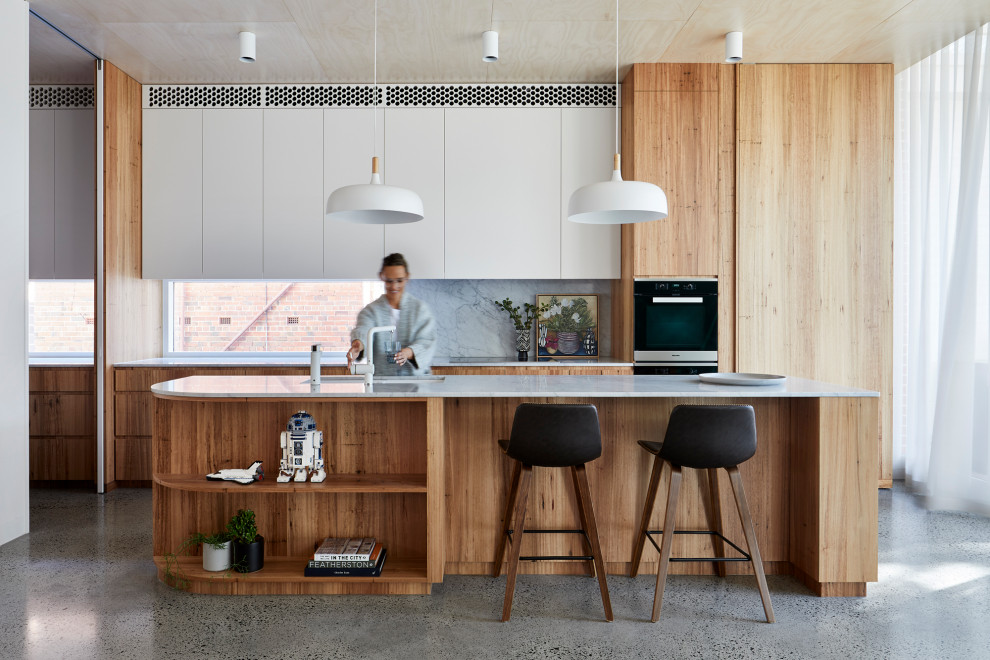 Large contemporary galley kitchen in Melbourne with an undermount sink, flat-panel cabinets, light wood cabinets, grey splashback, panelled appliances, terrazzo floors, with island, grey floor and white benchtop.