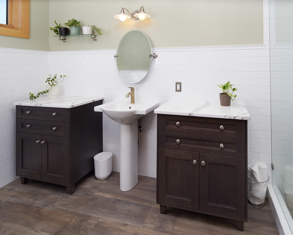 Corner shower - mid-sized transitional 3/4 white tile and subway tile medium tone wood floor and brown floor corner shower idea in Calgary with recessed-panel cabinets, dark wood cabinets, beige walls, a pedestal sink, quartz countertops and a hinged shower door