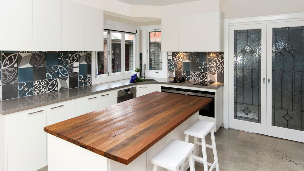 Design ideas for an eclectic kitchen in Toronto with flat-panel cabinets, white cabinets, wood benchtops, multi-coloured splashback, porcelain splashback, stainless steel appliances, concrete floors and with island.