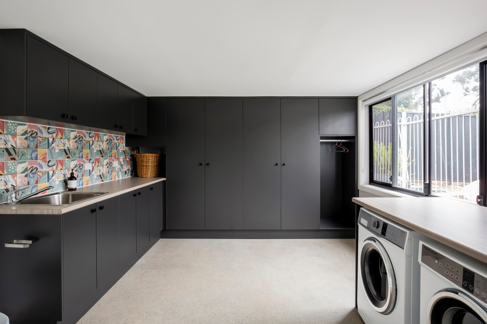 Mid-sized contemporary l-shaped utility room in Sydney with a drop-in sink, flat-panel cabinets, black cabinets, laminate benchtops, multi-coloured splashback, porcelain splashback, white walls, ceramic floors, a side-by-side washer and dryer, beige floor and beige benchtop.