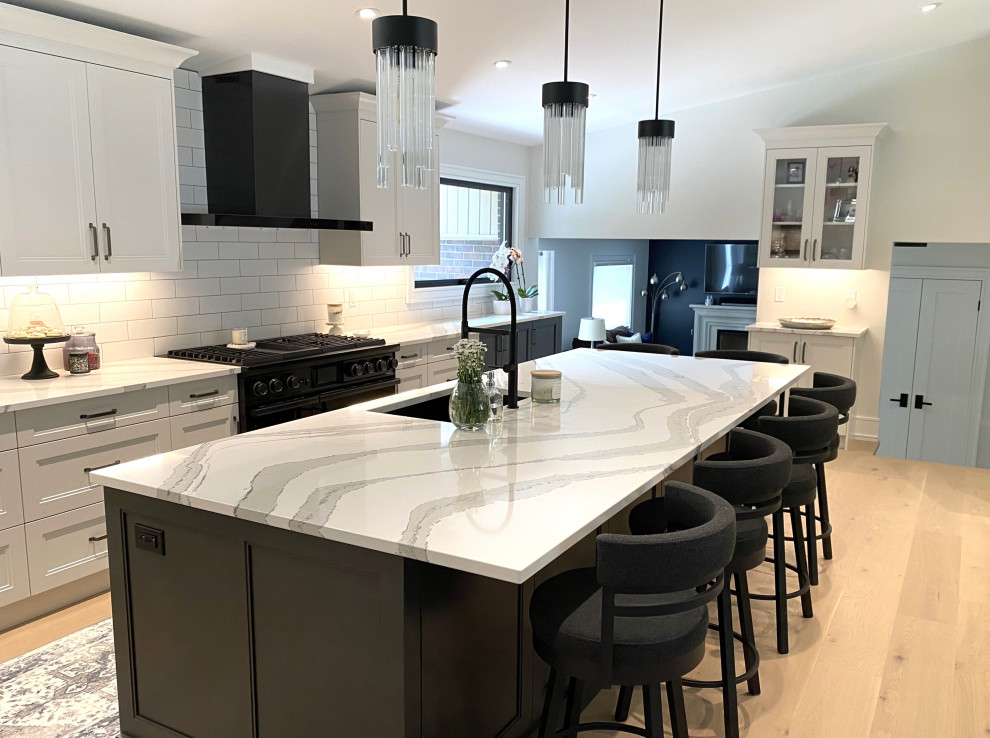 Open concept kitchen - large transitional l-shaped light wood floor and vaulted ceiling open concept kitchen idea in Toronto with an undermount sink, recessed-panel cabinets, white cabinets, quartz countertops, white backsplash, porcelain backsplash, stainless steel appliances, an island and white countertops