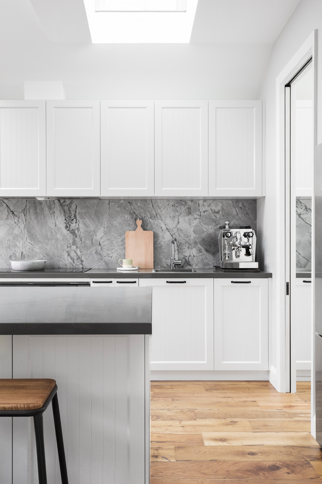 Photo of a large contemporary galley kitchen pantry in Melbourne with an undermount sink, shaker cabinets, white cabinets, quartz benchtops, grey splashback, stone slab splashback, stainless steel appliances, light hardwood floors, with island and grey benchtop.