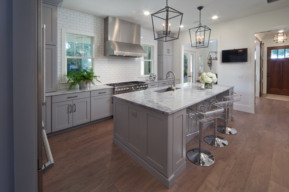 Open concept kitchen - mid-sized transitional l-shaped medium tone wood floor open concept kitchen idea in Orlando with granite countertops, white backsplash, ceramic backsplash, stainless steel appliances, an undermount sink, recessed-panel cabinets, gray cabinets and an island