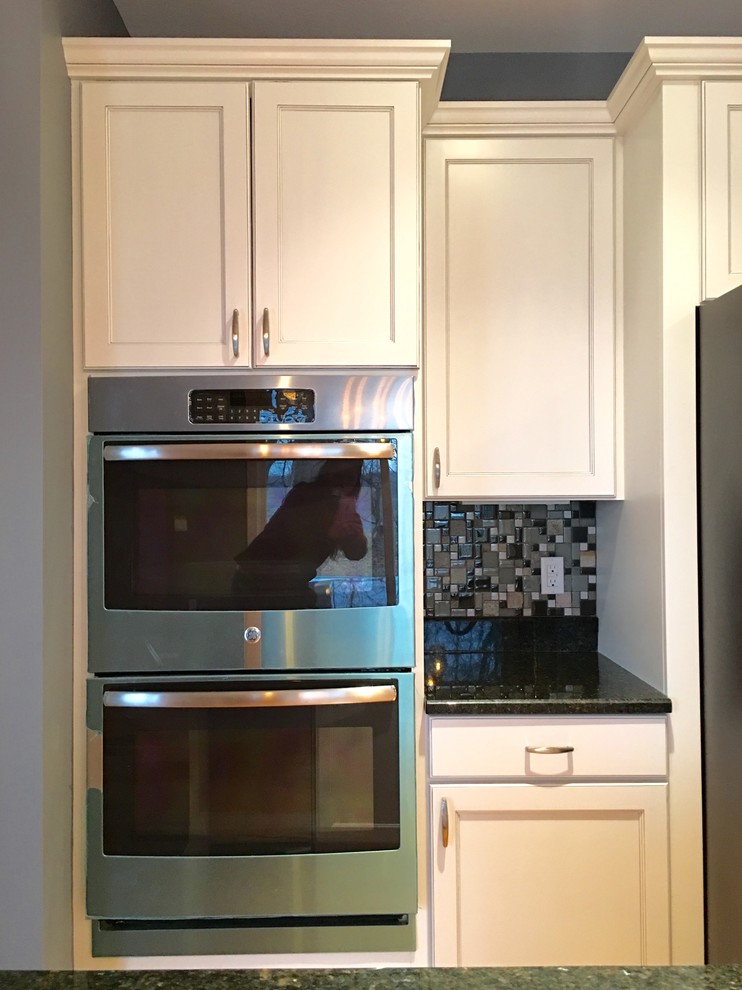 Inspiration for a large transitional l-shaped light wood floor eat-in kitchen remodel with an undermount sink, recessed-panel cabinets, white cabinets, granite countertops, multicolored backsplash, glass tile backsplash, stainless steel appliances and an island