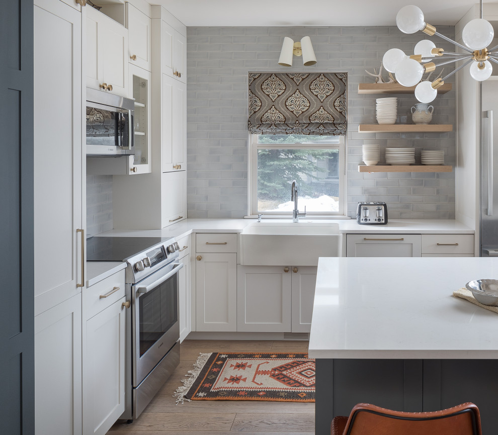 Inspiration for a small transitional l-shaped open plan kitchen in Denver with a farmhouse sink, shaker cabinets, grey cabinets, quartz benchtops, grey splashback, subway tile splashback, stainless steel appliances, medium hardwood floors, with island, white benchtop and beige floor.