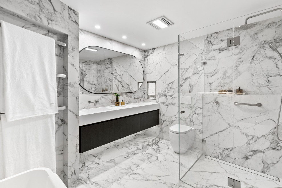 Cette image montre une grande salle de bain grise et noire et principale minimaliste avec des portes de placard noires, une baignoire indépendante, un carrelage noir et blanc, des carreaux de porcelaine, un mur blanc, un sol en carrelage de porcelaine, un lavabo intégré, un plan de toilette en surface solide, un sol blanc, un plan de toilette blanc, meuble double vasque, meuble-lavabo suspendu, un placard en trompe-l'oeil, une douche d'angle, WC à poser et une cabine de douche à porte battante.