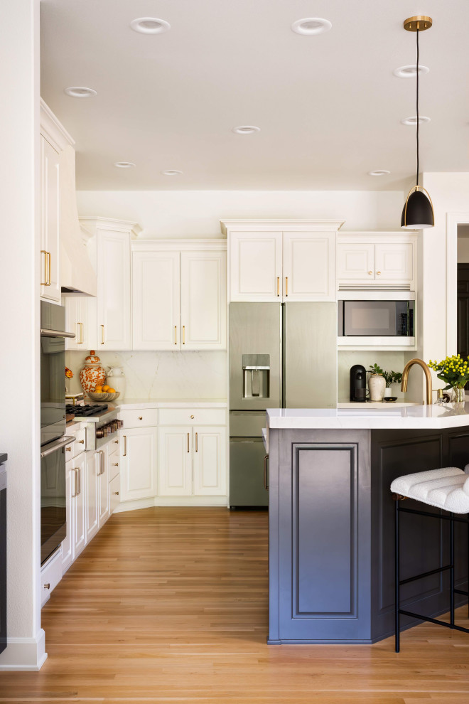 Inspiration for a mid-sized transitional l-shaped light wood floor and brown floor eat-in kitchen remodel in Portland with shaker cabinets, white cabinets, quartzite countertops, white backsplash, marble backsplash, an island, white countertops, a drop-in sink and stainless steel appliances