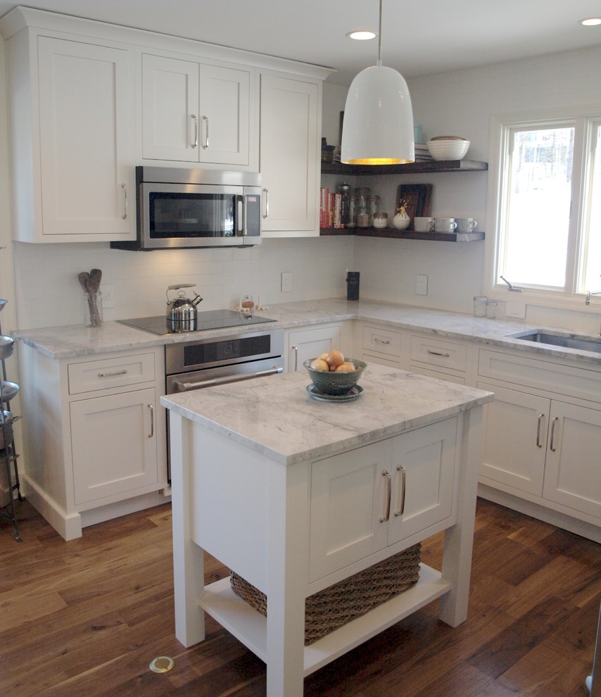 This is an example of a small country u-shaped eat-in kitchen in New York with a drop-in sink, white cabinets, white splashback, subway tile splashback, stainless steel appliances, dark hardwood floors, with island, white benchtop and shaker cabinets.