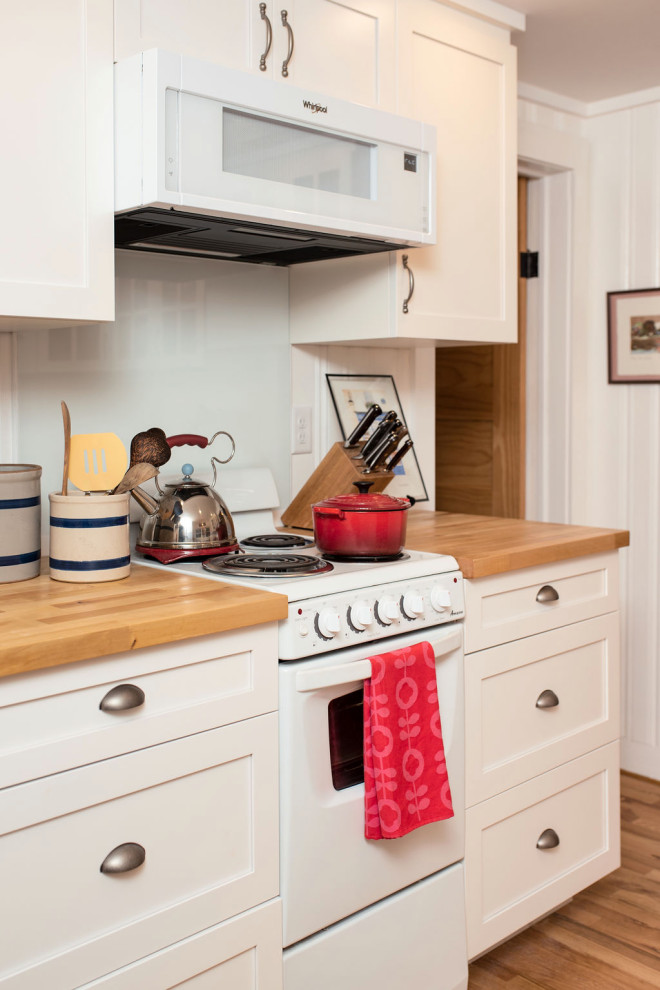 Small traditional galley separate kitchen in Other with a farmhouse sink, shaker cabinets, white cabinets, wood benchtops, white splashback, glass sheet splashback, white appliances, light hardwood floors, no island, brown floor and brown benchtop.