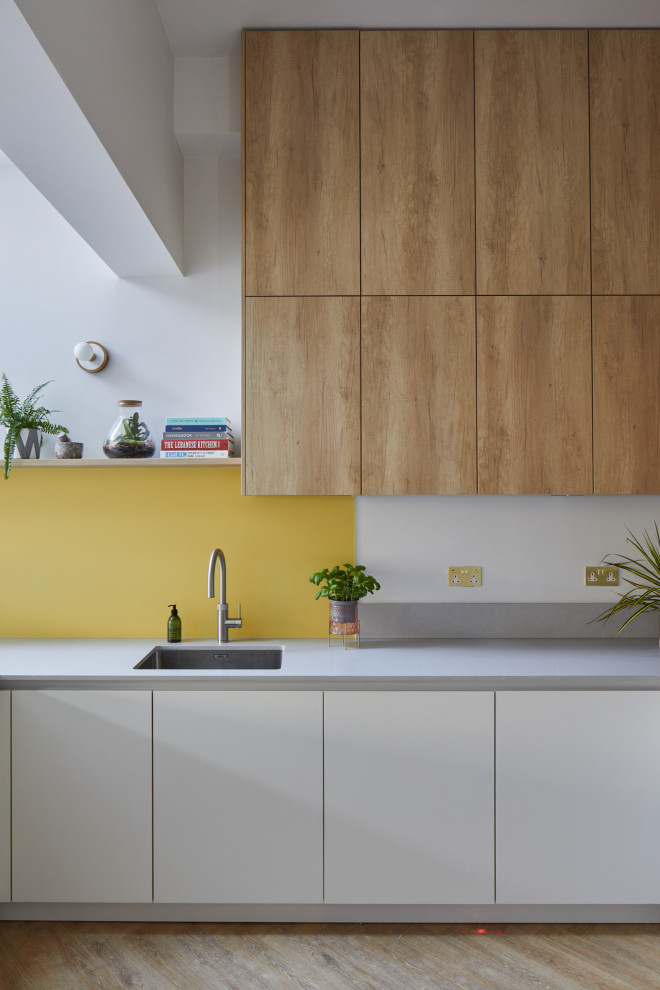 This is an example of a small modern u-shaped eat-in kitchen in London with an undermount sink, flat-panel cabinets, white cabinets, quartz benchtops, yellow splashback, glass sheet splashback, stainless steel appliances, medium hardwood floors, a peninsula, brown floor and white benchtop.