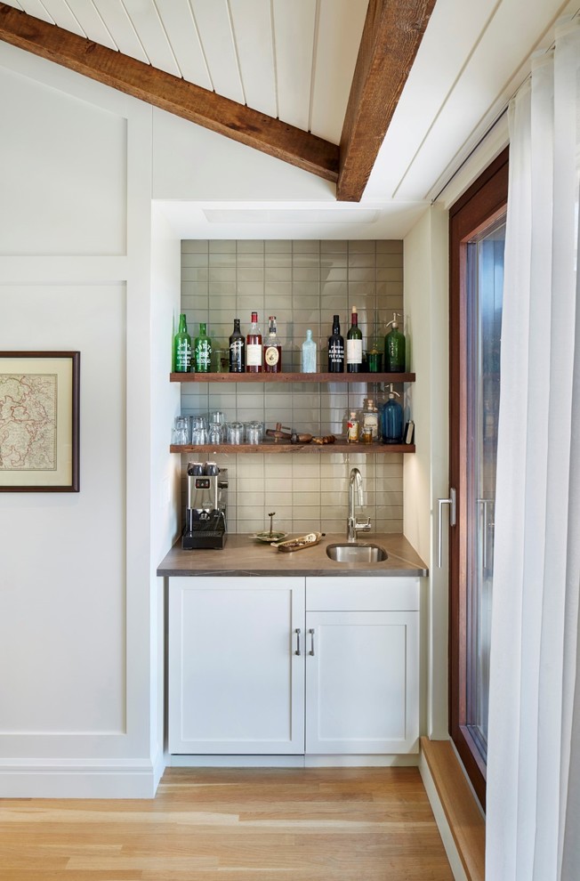 This is an example of a small transitional single-wall wet bar in New York with an undermount sink, grey splashback, light hardwood floors, shaker cabinets, white cabinets, marble benchtops, glass tile splashback and grey benchtop.