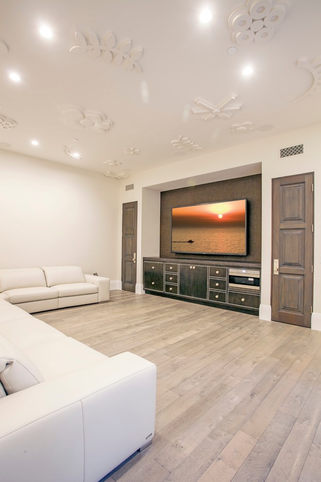 Mid-sized transitional open concept home theatre in Orange County with a wall-mounted tv, white walls and light hardwood floors.