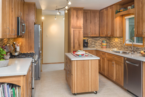 Compact rolling kitchen island with deep drawers and enclosed cabinet, matching warm-wood kitchen cabinets in a galley kitchen—adds organized storage and prep space