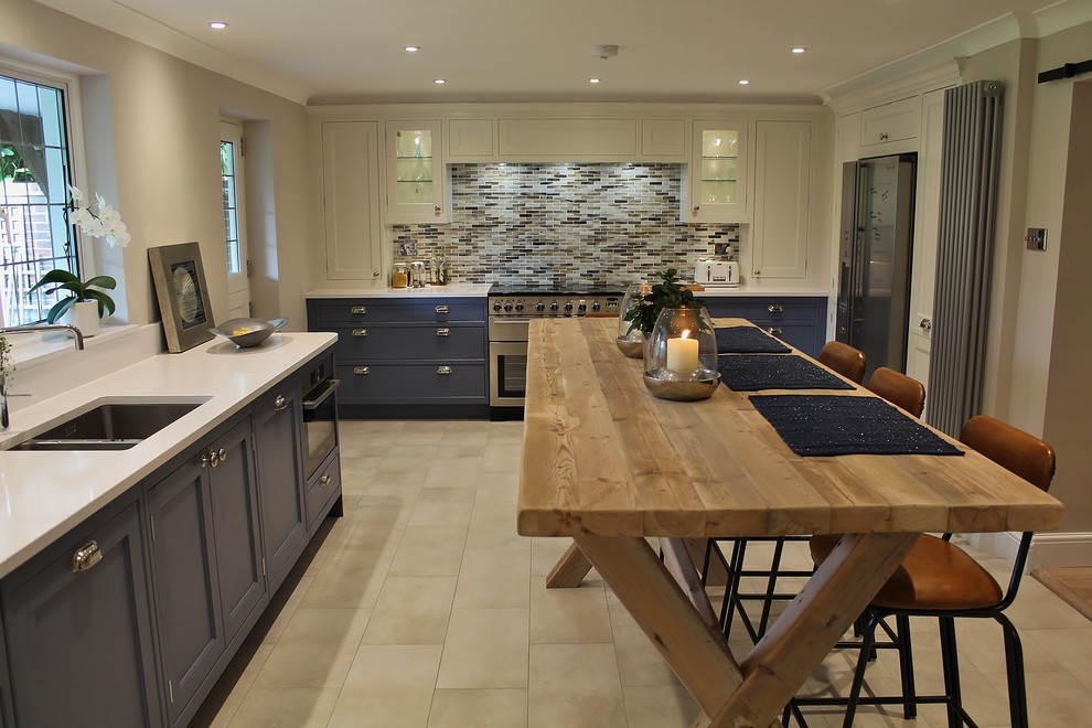 This is an example of a mid-sized transitional l-shaped eat-in kitchen in London with a drop-in sink, shaker cabinets, blue cabinets, quartzite benchtops, multi-coloured splashback, glass tile splashback, stainless steel appliances, ceramic floors and with island.