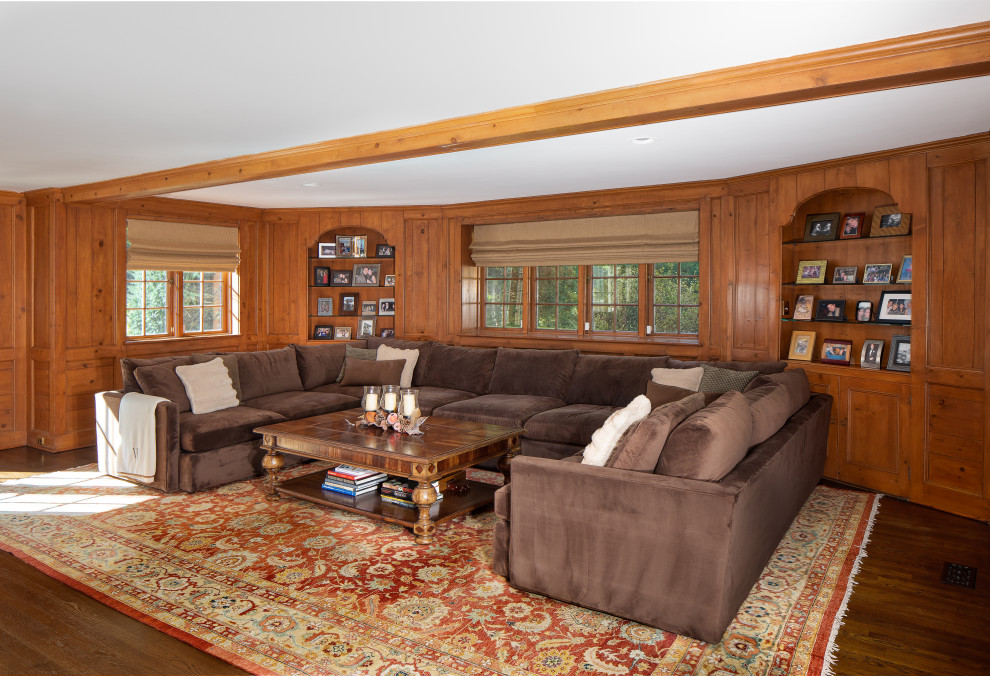 Cette image montre une grande salle de séjour traditionnelle fermée avec un mur marron, un sol en bois brun, une cheminée standard, un manteau de cheminée en bois et un sol marron.