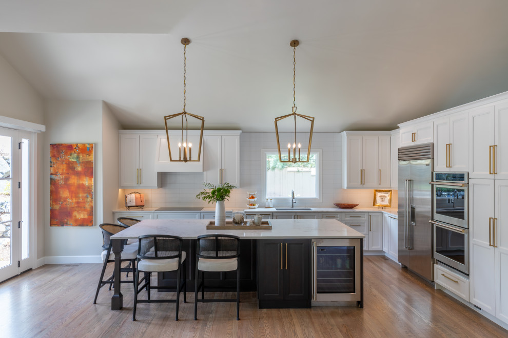 Example of a large transitional l-shaped medium tone wood floor, brown floor and vaulted ceiling open concept kitchen design in Denver with an undermount sink, raised-panel cabinets, white cabinets, quartz countertops, white backsplash, porcelain backsplash, stainless steel appliances, an island and white countertops