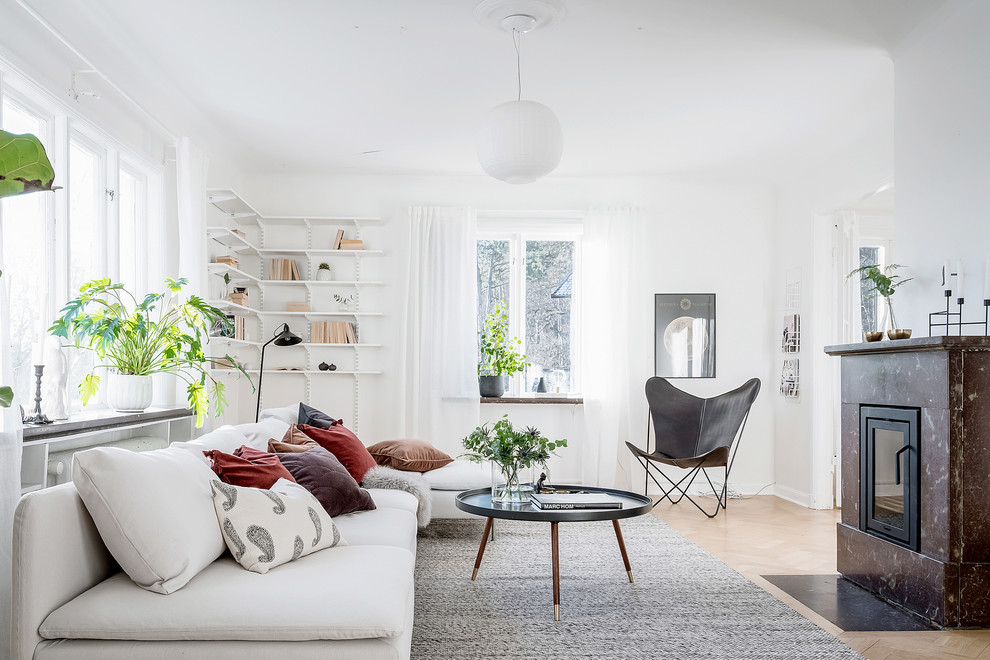 This is an example of a scandinavian formal enclosed living room in Gothenburg with white walls, light hardwood floors, a stone fireplace surround, beige floor, a standard fireplace and no tv.