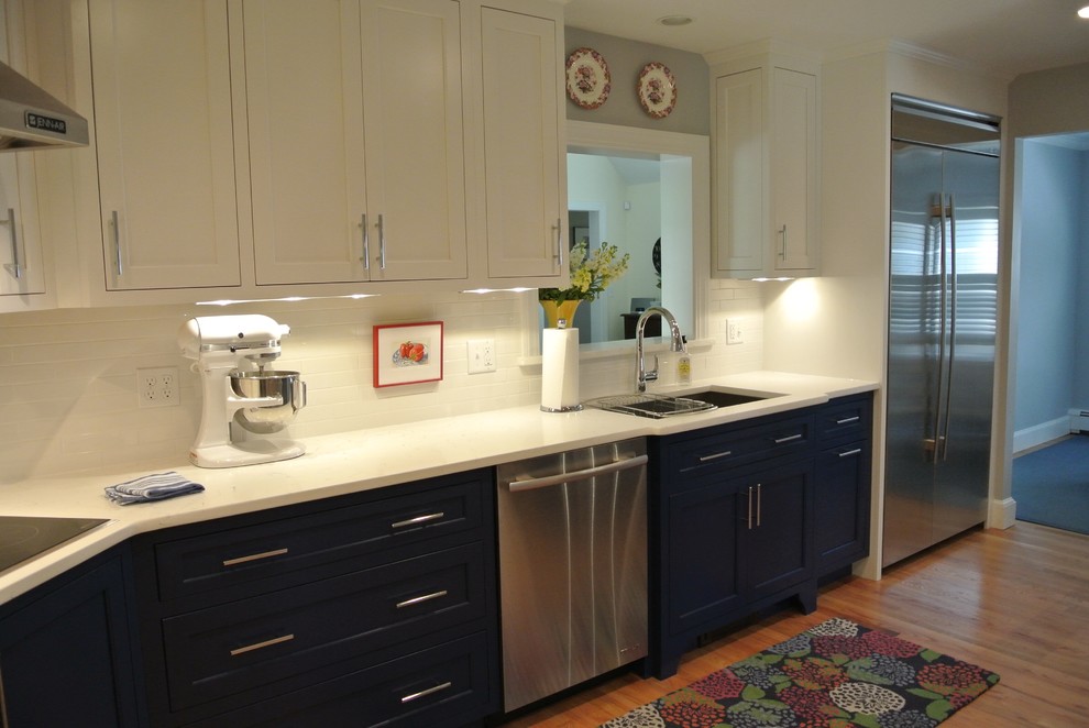 Transitional l-shaped medium tone wood floor kitchen photo in Boston with an undermount sink, shaker cabinets, blue cabinets, white backsplash, ceramic backsplash, stainless steel appliances and white countertops