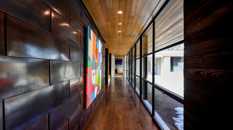 На фото: огромный коридор в стиле модернизм с разноцветными стенами, паркетным полом среднего тона, коричневым полом, деревянным потолком и панелями на части стены с