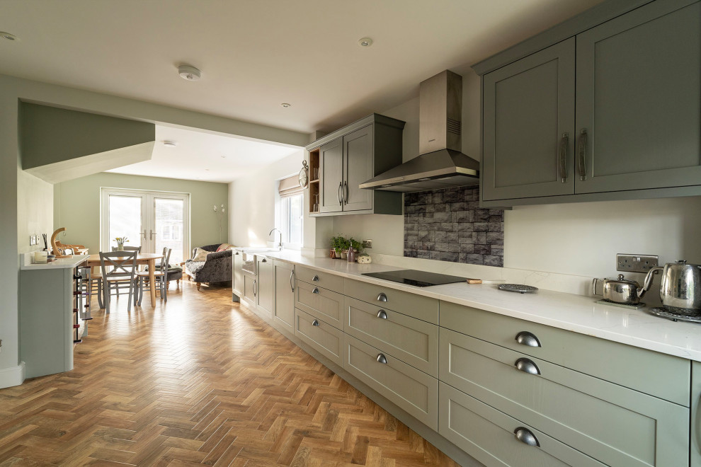 Mid-sized transitional single-wall kitchen pantry in Oxfordshire with a single-bowl sink, raised-panel cabinets, green cabinets, marble benchtops, white splashback, cement tile splashback, black appliances, medium hardwood floors, no island, brown floor and white benchtop.