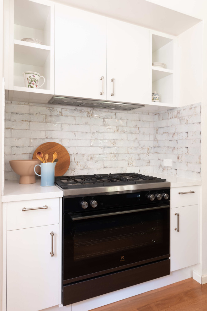 Exempel på ett mellanstort modernt vit vitt kök, med en dubbel diskho, vita skåp, vitt stänkskydd, glaspanel som stänkskydd, rostfria vitvaror, mellanmörkt trägolv och en köksö