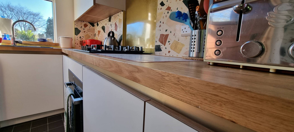 Идея дизайна: п-образная кухня среднего размера в скандинавском стиле с обеденным столом, одинарной мойкой, плоскими фасадами, белыми фасадами, деревянной столешницей, разноцветным фартуком, фартуком из керамической плитки, черной техникой, полом из керамической плитки, полуостровом, черным полом, коричневой столешницей и многоуровневым потолком