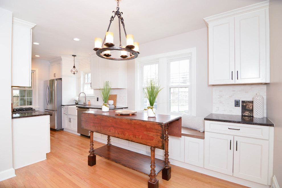 This is an example of a small country galley eat-in kitchen in DC Metro with a farmhouse sink, shaker cabinets, white cabinets, quartz benchtops, beige splashback, marble splashback, stainless steel appliances, light hardwood floors and no island.