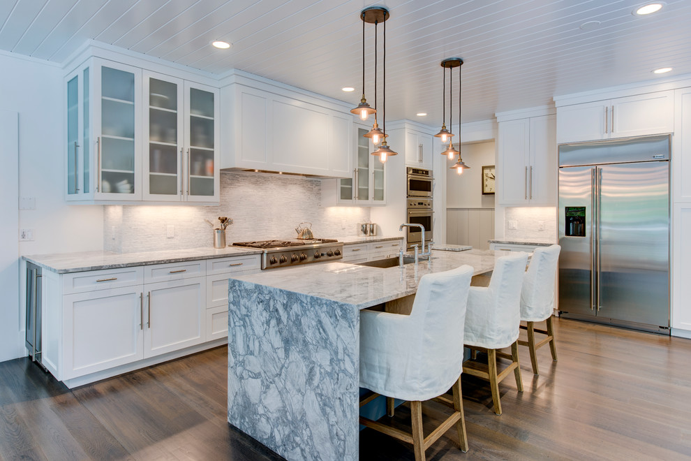 Large transitional l-shaped medium tone wood floor eat-in kitchen photo with a farmhouse sink, glass-front cabinets, white cabinets, quartzite countertops, white backsplash, ceramic backsplash, stainless steel appliances and an island