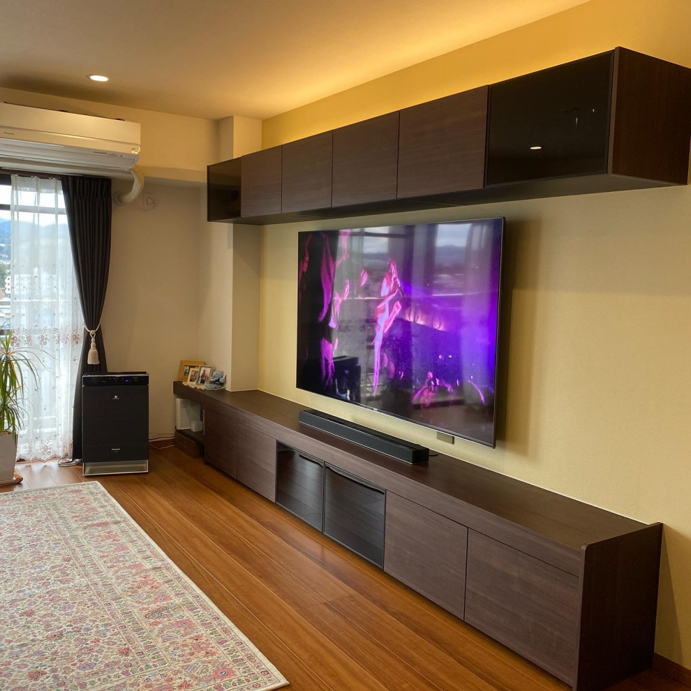 Foto på ett mellanstort vardagsrum, med gula väggar, plywoodgolv, en väggmonterad TV och brunt golv