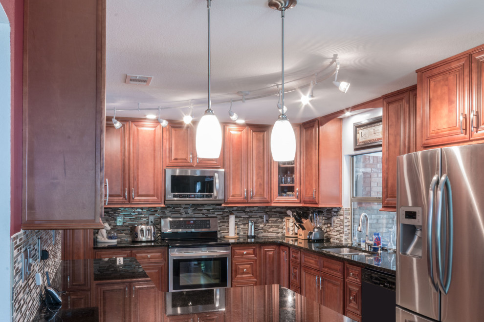 Kitchen - mid-sized l-shaped kitchen idea with an undermount sink, raised-panel cabinets, medium tone wood cabinets, granite countertops, glass tile backsplash, stainless steel appliances and black countertops