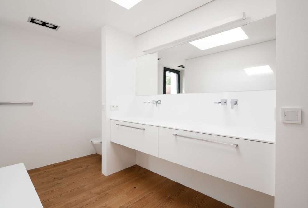 Mid-sized contemporary bathroom in Stuttgart with a trough sink, flat-panel cabinets, white cabinets, white walls and medium hardwood floors.