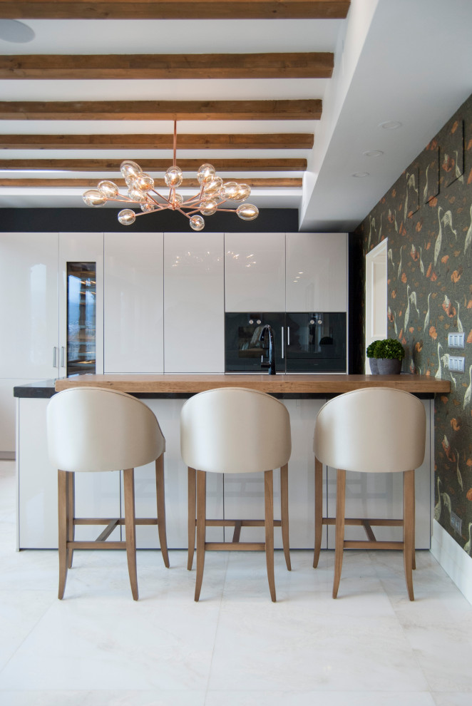 This is an example of a large contemporary single-wall open plan kitchen in Bilbao with an undermount sink, flat-panel cabinets, beige cabinets, quartzite benchtops, black appliances, marble floors, with island, beige floor, brown benchtop and exposed beam.