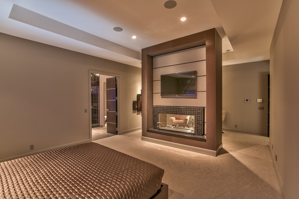 Large contemporary master bedroom in Omaha with grey walls, a two-sided fireplace, carpet, a tile fireplace surround and beige floor.