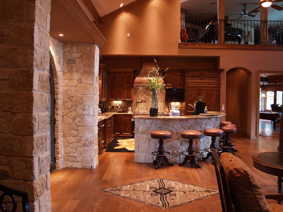 Example of a transitional l-shaped medium tone wood floor open concept kitchen design in Austin with raised-panel cabinets, medium tone wood cabinets, granite countertops, multicolored backsplash, glass tile backsplash, paneled appliances and an island