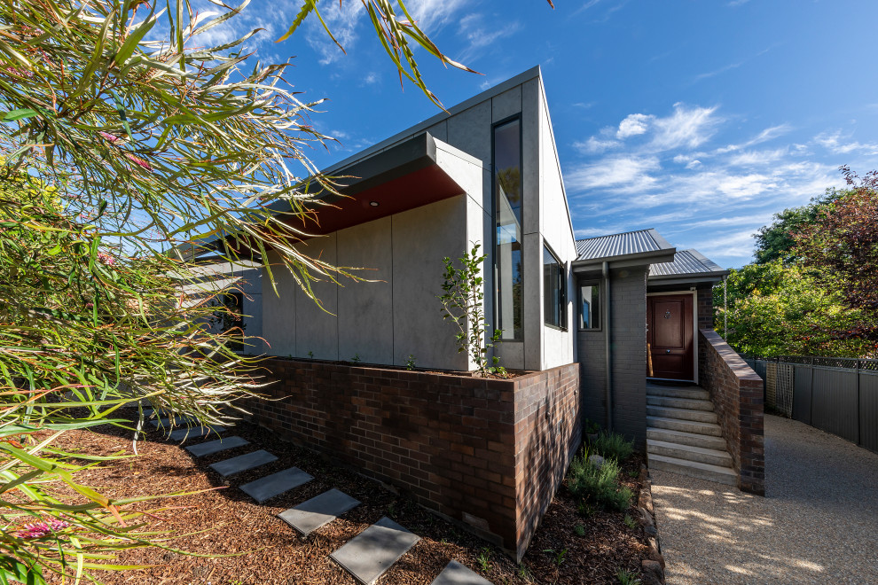 This is an example of a small one-storey house exterior in Canberra - Queanbeyan with concrete fiberboard siding, a butterfly roof and a metal roof.