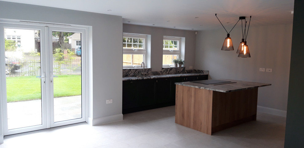 This is an example of a contemporary open plan kitchen in Dorset with green cabinets, quartzite benchtops, stainless steel appliances, with island and multi-coloured benchtop.