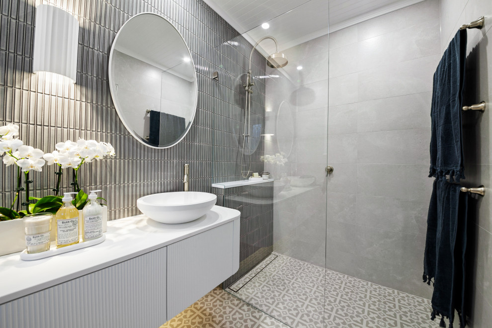 Inredning av ett mellanstort vit vitt badrum med dusch, med luckor med profilerade fronter, vita skåp, en dusch i en alkov, en toalettstol med hel cisternkåpa, flerfärgad kakel, keramikplattor, flerfärgade väggar, klinkergolv i keramik, ett fristående handfat, bänkskiva i akrylsten, grått golv och med dusch som är öppen