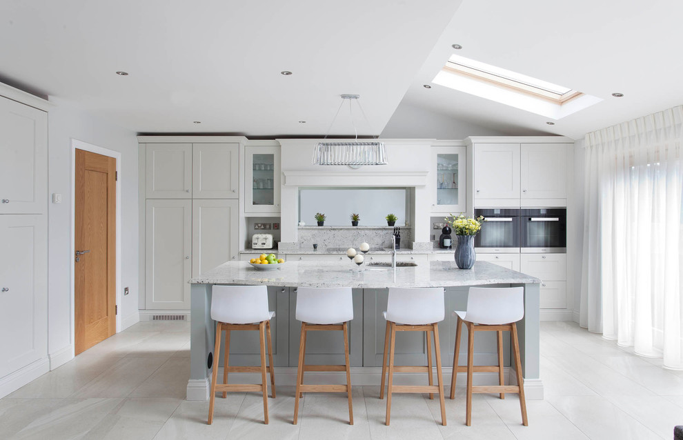 Large transitional l-shaped open plan kitchen in Dublin with an integrated sink, shaker cabinets, blue cabinets, granite benchtops, multi-coloured splashback, stone slab splashback, black appliances, ceramic floors and with island.