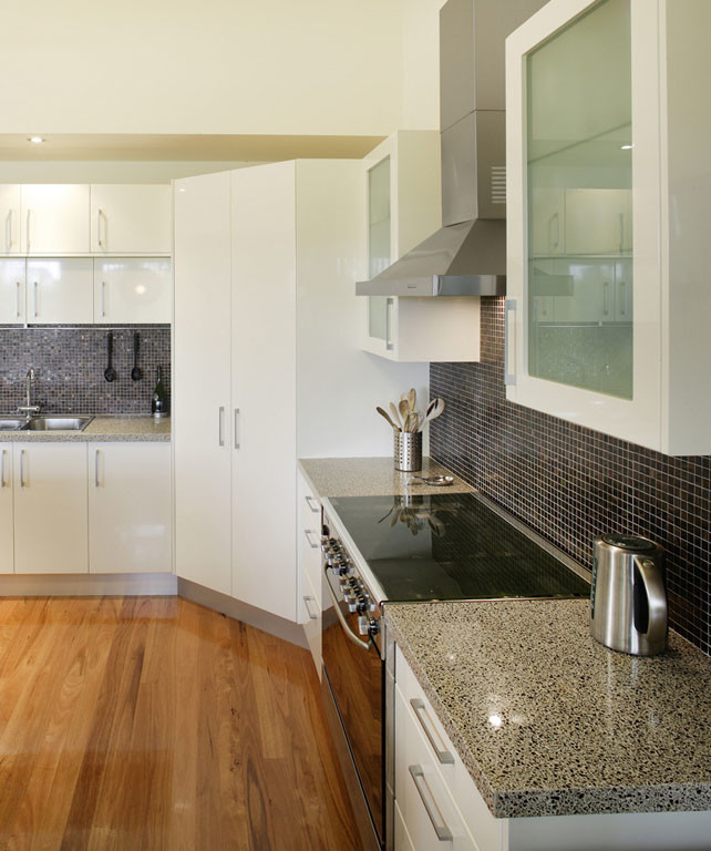 This is an example of a large transitional l-shaped separate kitchen in DC Metro with a drop-in sink, flat-panel cabinets, white cabinets, terrazzo benchtops, black splashback, mosaic tile splashback, stainless steel appliances, medium hardwood floors, with island and brown floor.